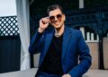 Man in blue suit and sun glasses sitting on a couch outside