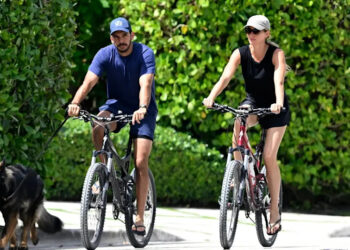 Joaquim Valente in a blue shirt rides a bike alongside Gisele Bündchen in a black shirt