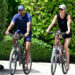 Joaquim Valente in a blue shirt rides a bike alongside Gisele Bündchen in a black shirt