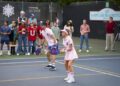 A still photo of two people in pink polo shirts on a pickleball court in action during a game