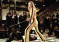 woman in a yellow outfit wielding a sword surrounded by attackers in suits