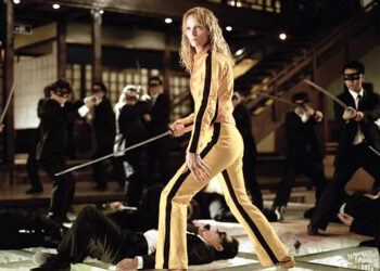 woman in a yellow outfit wielding a sword surrounded by attackers in suits