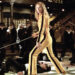 woman in a yellow outfit wielding a sword surrounded by attackers in suits