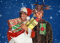 Andrew Ridgeley, dressed in a reindeer headdress and costume with a red dot on his nose, closes his eyes and purses his lips as George Michael, dressed in a white-furred Santa hat and coat and holding brightly wrapped Christmas presents, looks towards him. Snow falls on both of the men who are white-skinned brunettes.