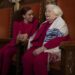 An older woman in a tallis sits in a synagogue with a friend.