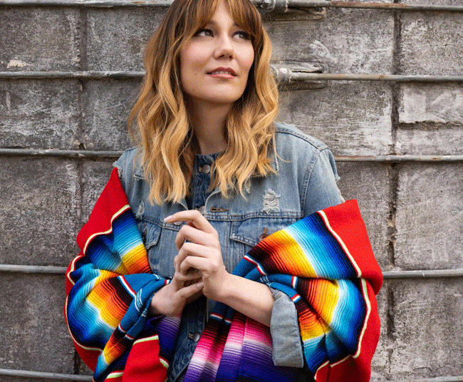 Molly Tuttle, wearing a denim jacket and brighly colored shawl, will perform at the Arlington Theatre, Sunday, Dec. 7 in support of her new album "So Long Little Miss Sunshine." (Ebru Yildiz photo)