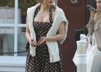 woman in a polka dot dress and sweater holding a phone