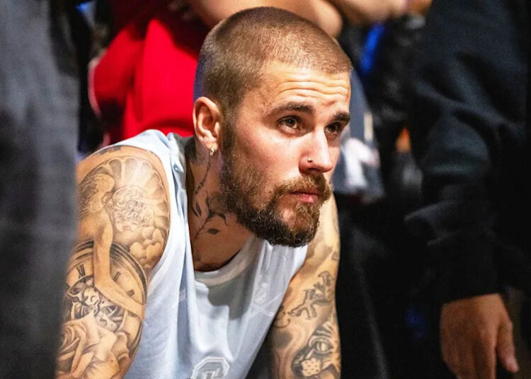 A close-up of Justin Bieber wearing a sleeveless white shirt looking reflective.