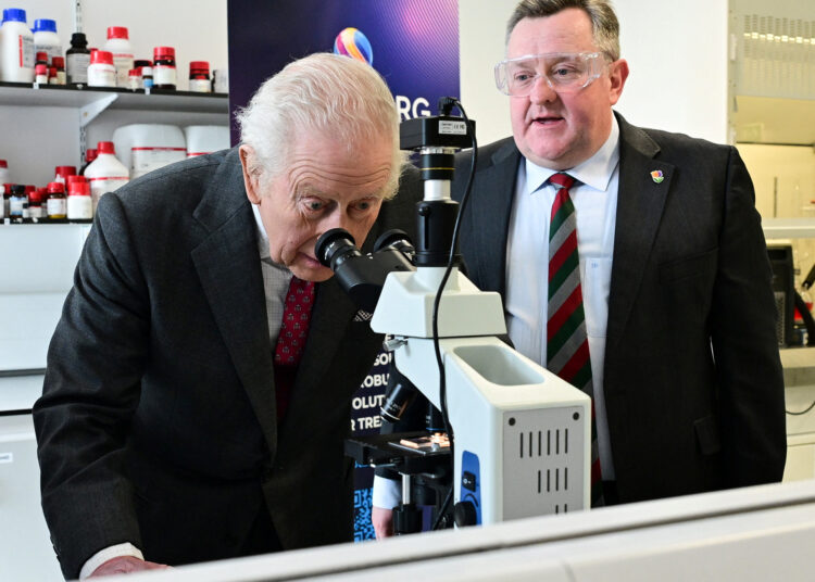 King Charles III looking through a microscope at a cancer research center.