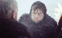 Two bearded men in fur-lined clothing look at each other intensely in a snowy setting, suggesting a dramatic or tense moment