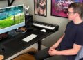 A man sitting in a computer chair watching a computer monitor with a game on it.