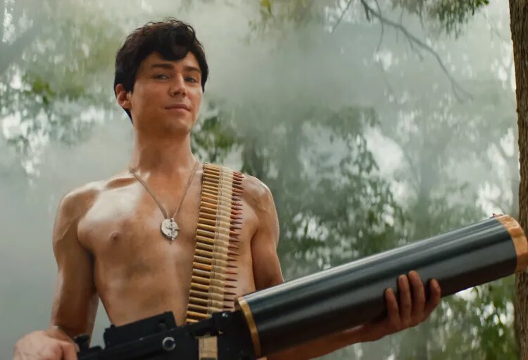 Miles Heizer as Cameron Cope, shirtless with an ammunition belt over his shoulder and a large weapon, in a misty forest.