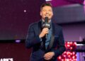 A man in a blue tuxedo holding a microphone near his mouth
