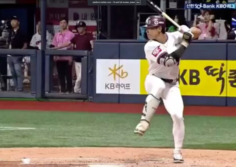 A baseball player in a white uniform with a maroon helmet and a bat in hand, standing at home plate, with "KB" and "KB LIFE" visible on the surrounding signage.
