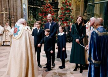 The royal family standing in front of a priest in a church