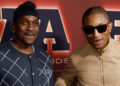 Pusha T and Pharrell Williams pose together at an event, both smiling. Pharrell wears sunglasses and a beige jacket.