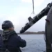 BBC Three men in hardhats onboard a ship launching  a SG-1 Fathom glider into the sea. It is lifted by a pulley and lowered into the water