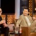 Two men sit next to each other in club chairs, laughing.