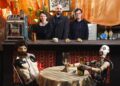 Three people stand behind a bar with two animatronics at a table before them.