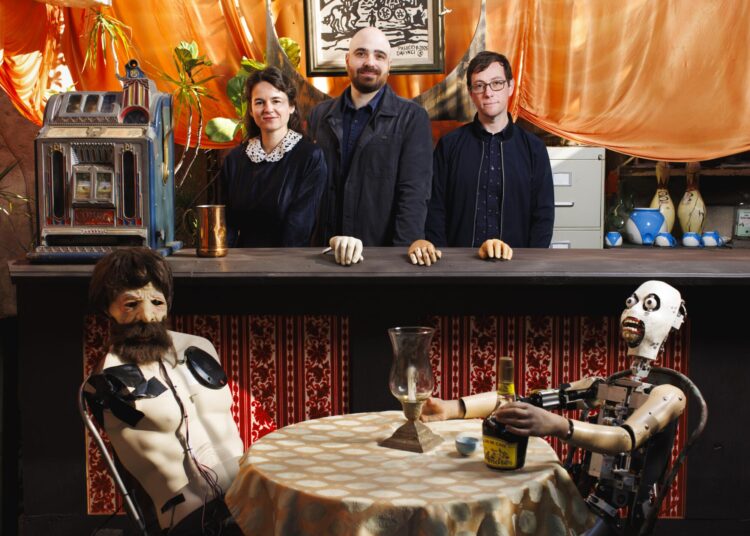 Three people stand behind a bar with two animatronics at a table before them.
