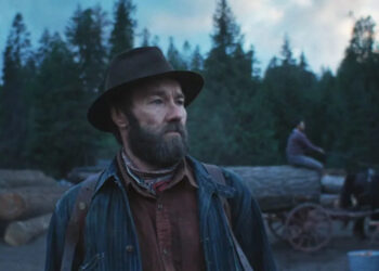 Joel Edgerton as Robert in Train Dreams, walking in a logging camp.