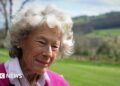 Dame Shân, with short grey hair and wearing a pink jumper and shirt.