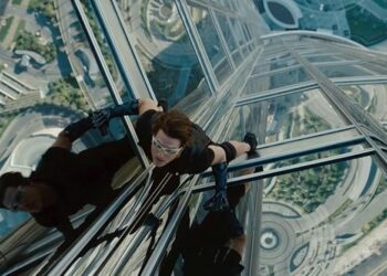 Looking down on Tom Cruise dressed in black climbing the outside of a very tall and modern building.
