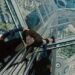 Looking down on Tom Cruise dressed in black climbing the outside of a very tall and modern building.