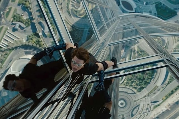 Looking down on Tom Cruise dressed in black climbing the outside of a very tall and modern building.