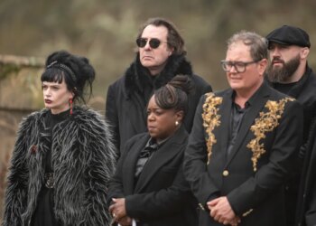 Five individuals from The Celebrity Traitors, dressed in dark clothing, stand outdoors in a somber group.