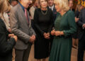 Queen Camilla wears a bright green dress and talks to a man in a suit