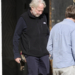 Timothy Busfield in a black vest and dark pants, accompanied by a man in a light blue shirt.