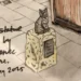Ama Menec An ink and pen sketch of the cat statue. The tabby cat is sitting on a low stone plinth on the pavement next to a wooden planter. A handwritten note reads: Susie statue design by Ama Menec Sculpture, January 2025.