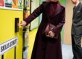 Duchess Sophie wearing a maroon coat and bag pressing a button on a colorful wall