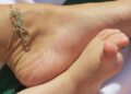 a closeup view of a foot and an infants foot next to each other with an anklet visible