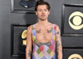 Harry Styles at an event, wearing a colorful, sleeveless checkered outfit. Black background with awards and CBS logo.