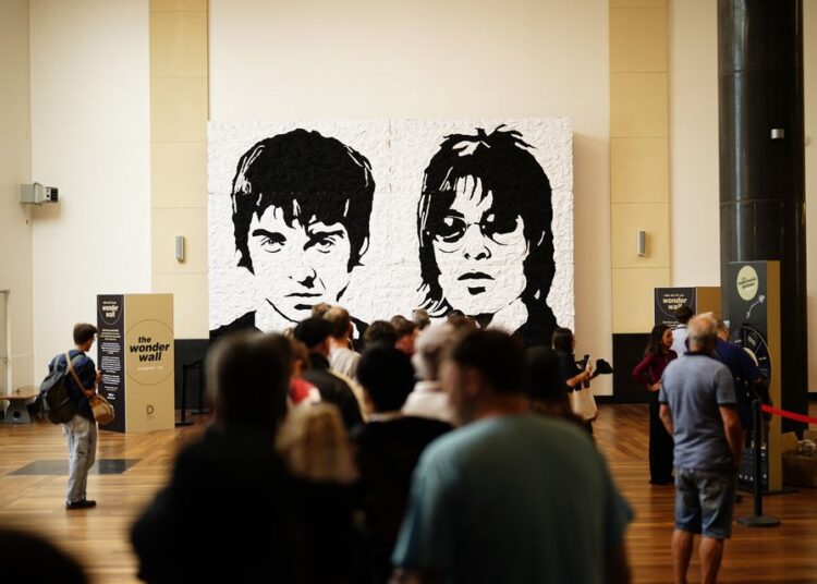 Oasis fans take photos in front of the Wonder Wall – a mural made out of 3,000 black and white bucket hats depicting Liam and Noel Gallagher – in Cardiff, ahead of the first show in the band’s long-awaited reunion tour (Jordan Pettitt/PA)