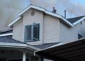 A man seen on a rooftop from a distance as smoke clouds billow above.