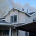A man seen on a rooftop from a distance as smoke clouds billow above.