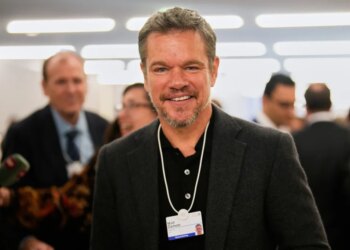 Actor Matt Damon smiling while wearing a conference badge around his neck at the World Economic Forum.