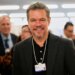 Actor Matt Damon smiling while wearing a conference badge around his neck at the World Economic Forum.