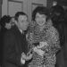 A black and white photograph of a man in a dark suit with a laughing woman in a leopard-print coat.