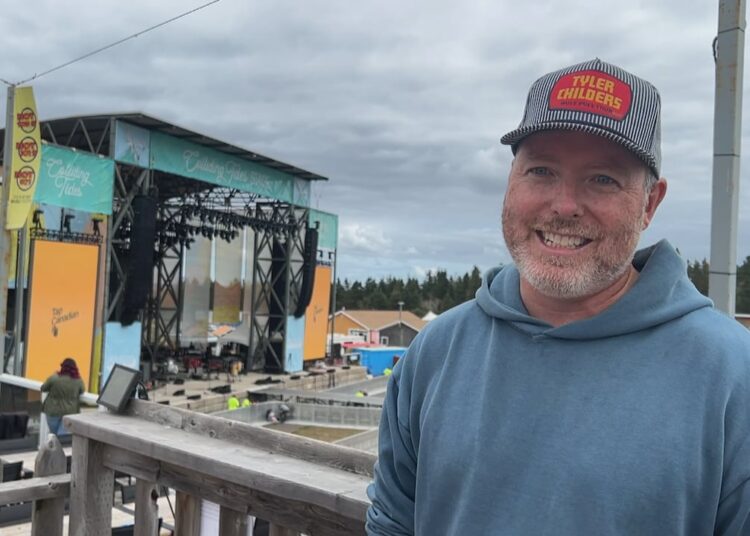 A man in a blue hoodie with a stage behind him.