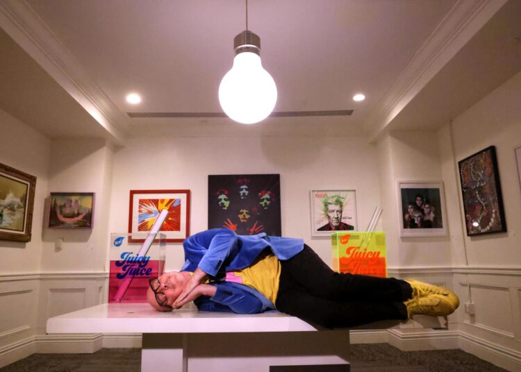 A man lays on a bench in an art gallery.