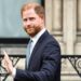 Prince Harry - a slightly-balding man with red hair and a red beard waves as he steps into a dark coloured car. He wears a pale blue shirt and a navy blue suit, with a brown beaded bracelet.