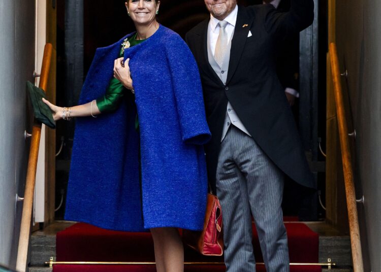 Queen Maxima wearing a blue coat standing on stairs next to King Willem-Alexander
