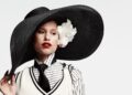 raye wearing an oversized black hat with a floral decoration