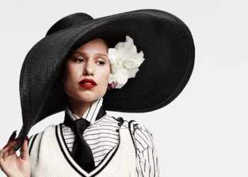raye wearing an oversized black hat with a floral decoration