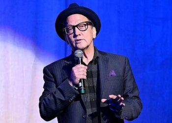 Rob Schneider holding a microphone on stage