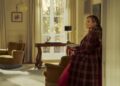Sarah Jessica Parker, as Carrie Bradshaw, stands against a wall in her living room in "And Just Like That."